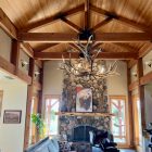 Yellowstone Elk Antler Chandelier hanging above a rustic living room with a stone fireplace and bear painting