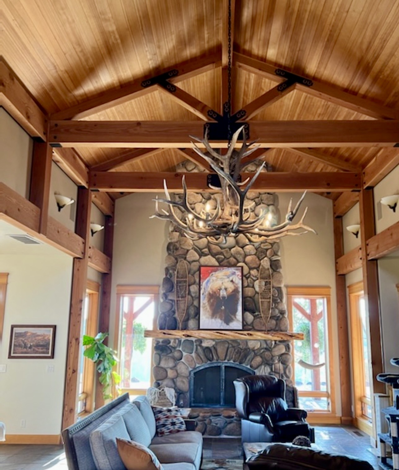 Yellowstone Elk Antler Chandelier hanging above a rustic living room with a stone fireplace and bear painting