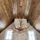 Yellowstone Elk Antler Chandelier hanging beneath a peaked wood ceiling above a stone chimney
