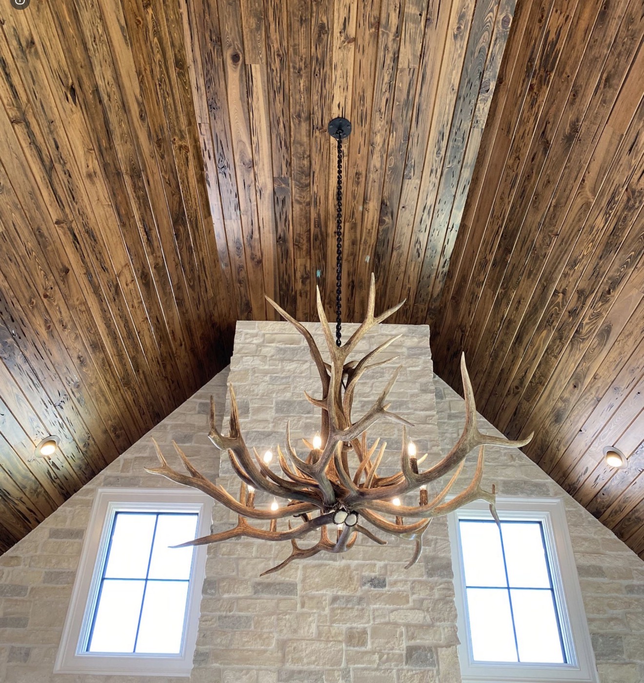 Yellowstone Elk Antler Chandelier hanging beneath a peaked wood ceiling above a stone chimney