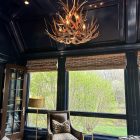 Deerlodge mule deer antler chandelier installed in a navy blue paneled sitting room with woven window shades