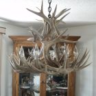 Sphinx Whitetail Antler Chandelier hanging over a rustic dining table with a stone fireplace in the background