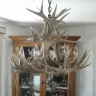 Two Tier Whitetail Antler Chandelier hanging over a rustic dining table with a stone fireplace in the background