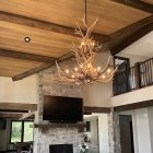 Selway 2-tier elk antler chandelier hanging over a stone fireplace with a mounted TV