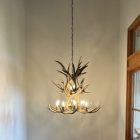 Aspen 2-tier mule deer antler chandelier hanging in a tall entryway with lit candle-style bulbs