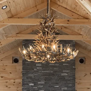 XL 6 tier whitetail antler chandelier installed above a stone fireplace in a vaulted wood-beam great room