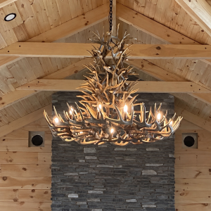XL 6 tier whitetail antler chandelier installed above a stone fireplace in a vaulted wood-beam great room
