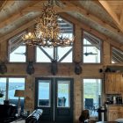 XL 6 tier whitetail antler chandelier installed over a vaulted great room with wood beams, mounted deer heads, and a lake view