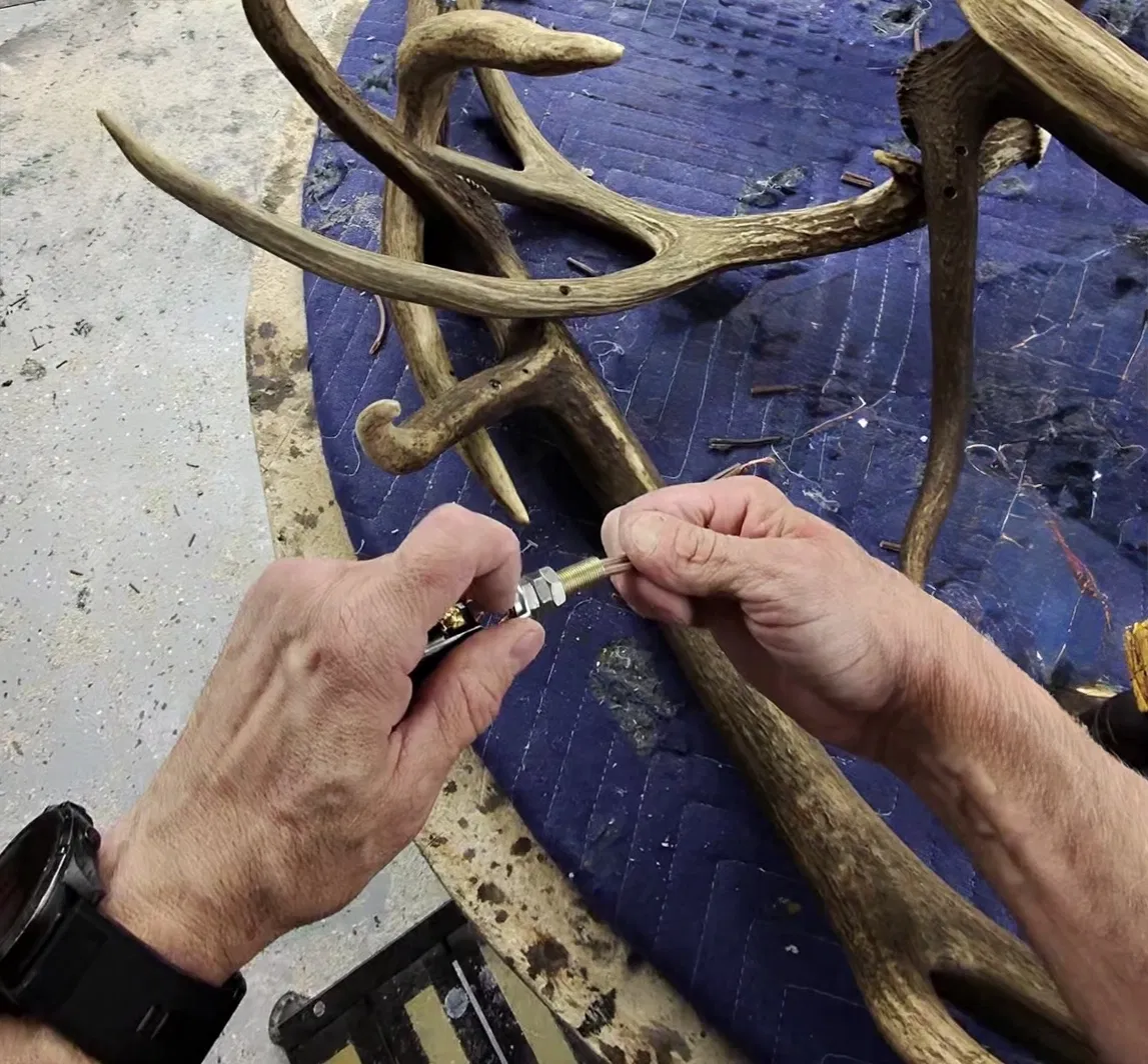 Hands fitting threaded hardware and wiring into a drilled elk antler during UL Listed antler chandelier assembly