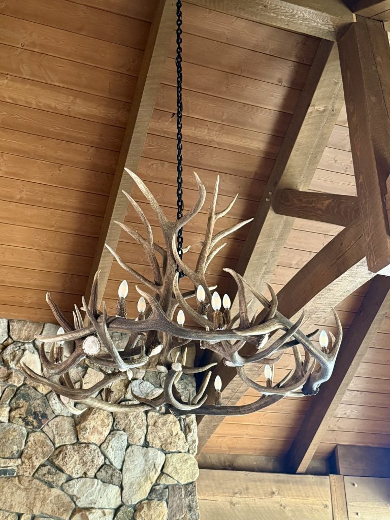 Close view of the 12-light Big Sky elk and mule deer antler chandelier beside the stone fireplace at Spirit Ranch