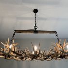 Luxury whitetail antler rectangular chandelier hanging in a kitchen, lit, close view