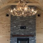 XL 6 tier whitetail antler chandelier installed above a stone fireplace in a vaulted wood-beam great room