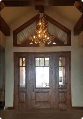 Custom antler chandelier installed above a wooden entryway door in a vaulted two-story foyer