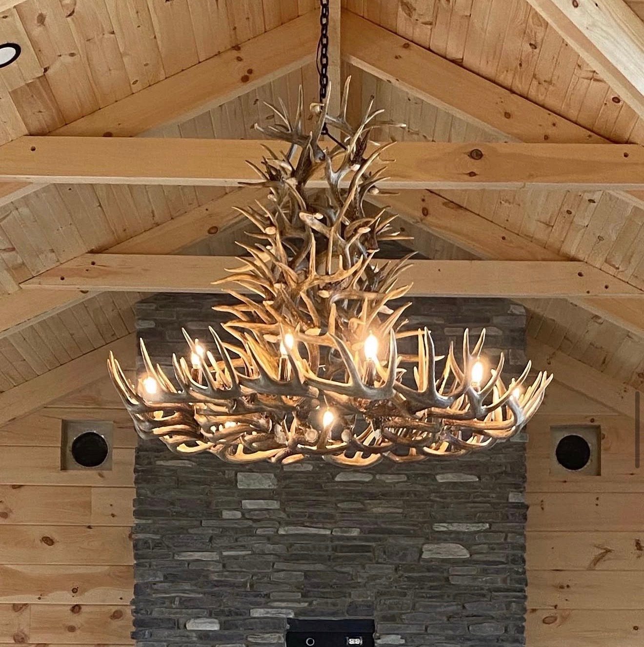 Chain-hung antler chandelier installed on a vaulted wood ceiling above a stone fireplace