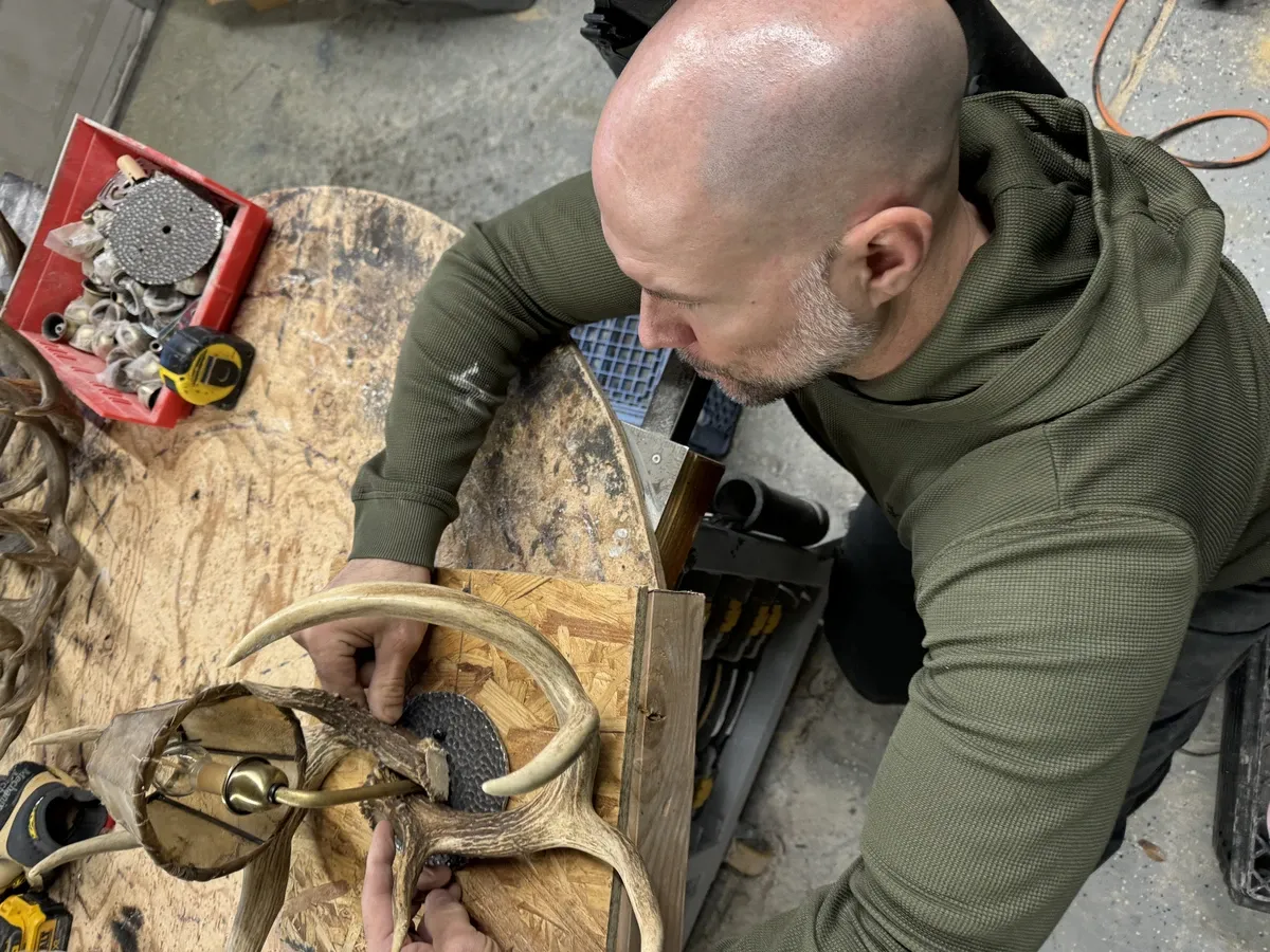 Craftsman sorting and selecting raw shed antlers at a workshop bench during custom chandelier design