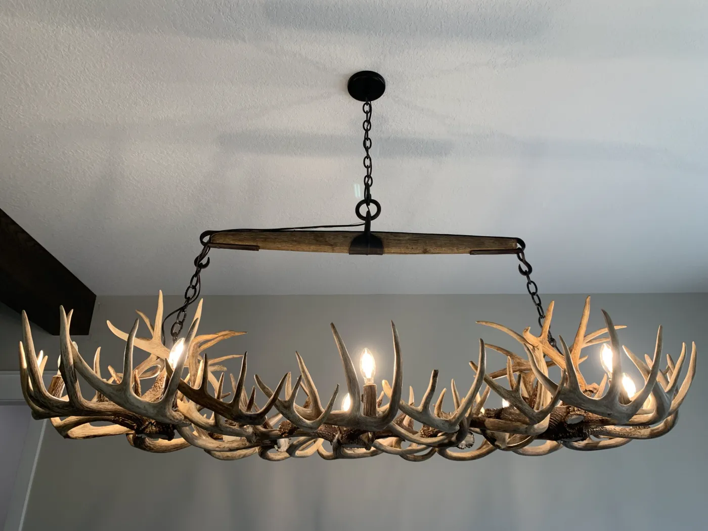 Linear antler chandelier hung from a wood crossbeam and chains with lit candle-style bulbs