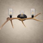 The Ridgeline elk antler 3-light wall light: a single shed elk antler mounted horizontally with three seeded glass cylinders and filament bulbs on a hammered steel back