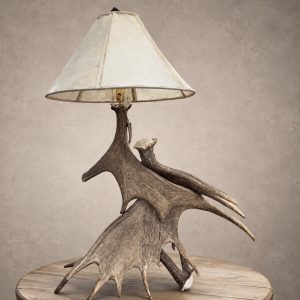 Kenai moose antler table lamp with stacked moose antler paddles and a laced rawhide shade on a wood side table