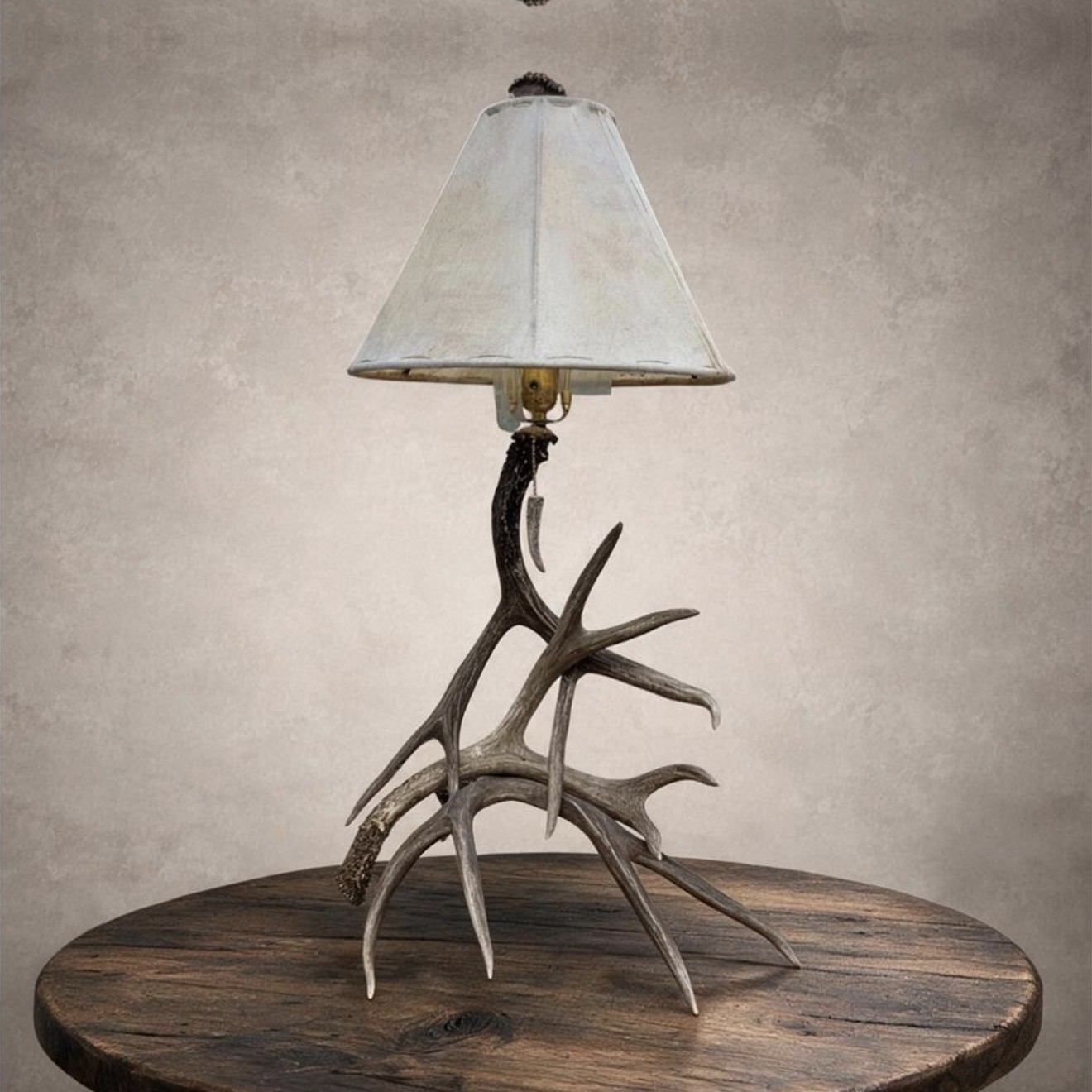 Mule Deer Antler Table Lamp – Madison Mule deer antler table lamp – Madison: real mule deer antler base with a rawhide shade and antler-tip pull chain, on a wood side table