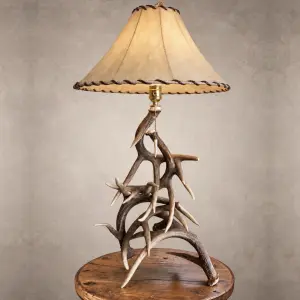 Whitetail antler table lamp – Silverbow: interlocking whitetail deer antler base with a laced rawhide shade and brass pull-chain socket, on a wood side table