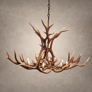 Wilderness elk antler chandelier lit with candle-style bulbs, hanging from a black chain against a textured gray backdrop