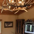 Yellowstone elk antler chandelier lit in a rustic living room beneath a wood plank ceiling